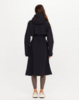 The Upside James Hooded trench coat in black, shown from the back, paired with patterned leggings.
