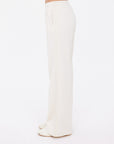A person is shown standing sideways against a plain white background, wearing The Upside’s NAVAR MARNIE WIDE LEG PANT in cream paired with open-toe sandals.