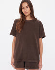 A woman with long brown hair models the SOHO EVA CREW TEE by Citizens Of Humanity/AGOLDE—a loose-fitting, short-sleeved crew neck t-shirt with matching brown shorts—against a plain white background.