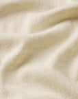 A close-up of The Knit Plus One Tee by FRAME shows its cream-colored, textured fabric with gentle folds and a nubby surface, capturing the relaxed luxury of this silk-inspired tee.