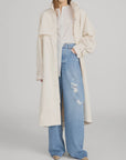 A woman wears FRAME’s The Field Trench over a white blouse and high-waisted, wide-leg distressed jeans, styled with beige pointed-toe shoes. Her face is partially out of frame.