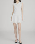 A woman models The Embroidered Day Dress by FRAME—a romantic sleeveless design with a white collar and lace trim at the hem and sides—against a plain light background, styled with black pointed-toe heels.