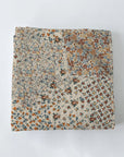The Winchester Orange Quilt by Faire is a folded Texas-made patchwork quilt with small floral patterns in earthy brown, blue, orange, and beige tones, shown on a plain white background.