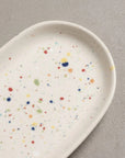 Faire White Mini Tray, oval ceramic tray with a multicolored paint splatter pattern by Bungalow Furniture & Accessories.