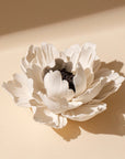 The Faire Ceramic Anemone Incense Holder features delicate, layered white petals and a dark textured center, evoking traditional Chinese artistry. It rests on a soft beige surface under gentle lighting.