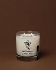 Anti-Pumpkin two-wick candle in a clear glass jar featuring a pumpkin-cowboy illustration from Bungalow.