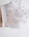 A hand holds up Faire's Blossom Breeze Sheer Floral Ankle Socks, featuring thin, ribbed, slightly transparent fabric with delicate pink and green floral patterns—ideal for those wanting lightweight, breathable socks with a feminine touch.