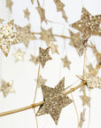 Close-up of Faire’s Gold Sparkle Star Chandelier, featuring glittery gold stars suspended from thin wires for a whimsical, pajaki-inspired decoration against a light background.