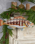 Walleye fish wall decor by The Faire hangs above a white mantel with greenery and candles for a cozy accent.