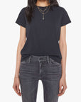 A woman wears Mother’s The Lil Goodie Goodie Tee in plain black, tucked into faded black jeans with layered gold necklaces and bracelets, standing against a white background.
