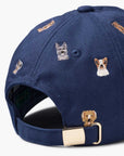 The Faire Dog Days Baseball Cap is navy blue with an adjustable strap, metal buckle, and embroidered dog faces on the back.