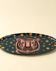 The Indaba Tiger Spot Tray features a dark background, orange polka dots, and a pink tiger face at the center, bringing a playful touch to your décor. Perfect as an accent piece when displayed on any plain surface.