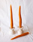 Three Faire Carrot Beeswax Candles are displayed: two upright in white holders and one lying down, all shown against a plain white background.