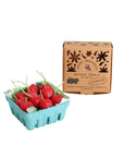 A blue carton containing cherry-shaped candles sits beside a brown box labeled “Faire Cherry Beeswax Candles,” decorated with simple plant doodles and handwritten-style text.