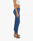 A person wearing a white sleeveless top, Mother Mid Rise Dazzler Ankle Fray jeans, and black strappy high-heeled sandals stands sideways against a plain white background.