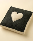 The Indaba Cream Heart Wall Plaque is a square handmade felt decor piece with black sides, a white bottom, and a white heart in the center—displayed on light beige, perfect as unique heart wall art.