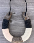 The Lucky Horseshoe by Faire is an upcycled horseshoe wrapped in black, gray, and white yarn, hanging by a black cord against a rustic wooden backdrop—a unique personalized gift.