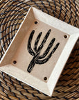 The Saguaro Soap Dish, a handmade piece with a black sgraffito cactus design and four drainage holes, rests on a woven spiral-patterned placemat.