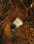 High Horse candle and fragrance bottle displayed on brown leather fringe chaps over rocky ground.
