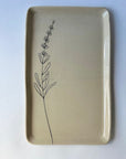 The CSF Tray by Faire is a rectangular beige ceramic plate featuring a simple black line drawing of a lavender sprig on the left, set against a white background for an elegant and calming touch.