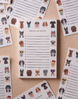 The Dog Days Notepad by Faire features cute dog faces along the top and bottom. Multiple tear-off sheets are shown on a neutral fabric, each perfect for jotting down playful to-do lists.