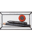 The Faire Glass Valet Tray neatly holds a red eraser, a black woodless pencil, and a sharpened black pencil with white text, offering a sleek and organized storage solution.
