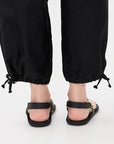 Black adjustable Flowze FLO sandals paired with drawstring pants, back view on a white background.