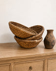 Two stacked vintage French antique baskets and a rustic ceramic vase on a light wood surface from Bungalow Furniture.