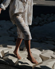 A person in Cissa's The Summer Pencil Skirt walks barefoot on large white geometric blocks, sandals in hand, with dark shadows behind.