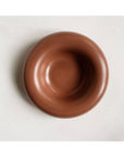The Faire Gyrus Pocket Tray—a round, smooth, brown ceramic bowl with a wide rim—rests on white fabric atop a concrete tray, seen from above.
