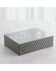 The Interwoven Box LG by Global Views features a rectangular shape with a grey and white geometric pattern, ideal for decorative storage. Shown on a light surface with white curtains in the background.