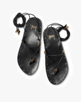 A pair of black leather Koha Sandals by Beek, featuring adjustable ankle-tie laces, gold bead accents, and metal studs around the edges, displayed on a white background. "Beek" is printed in gold on each insole.