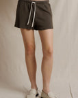 Perfectwhitetee Layla Terry Shorts in dark olive styled with cream loafers, set against a neutral beige fabric backdrop.