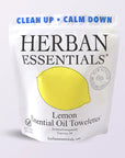 A white Faire pouch labeled "Lemon Towelettes - 20 Individual Essential Oil Wipes" features a lemon illustration, blue "CLEAN UP • CALM DOWN" text, and notes new recyclable bags. Citrus-scented wipes are individually wrapped for freshness.