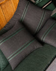 Leo Linen Pillows with green stripes by Libeco Home displayed on a green bench against a wooden wall.