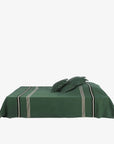 Green coverlet with black and white stripes and two matching pillows by Libeco Home, styled on a white bed.