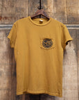 The Pocket Tee MadeWorn Records by Made Worn is a unisex cotton t-shirt in mustard yellow, featuring a front pocket and circular "MW RECORDS" logo. Shown on a wooden hanger against a rustic background. Made in USA.