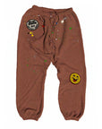 MadeWorn P.E. Sweatpants by Made Worn: heavyweight brown French terry joggers with elastic cuffs, colorful paint splatters, a round "MADE WORN 1971 ARTIST SH*T" patch on the left thigh, and a yellow smiley face patch on the right knee. Unisex fit.
