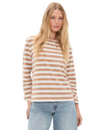 A woman with long blonde hair wears the MILLS POND STRIPED T by Denimist— a beige and white striped lightweight jersey tee—paired with light blue jeans, standing against a plain white background.