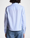 A person is seen from the back wearing The Belle by Cissa—a light blue, relaxed-fit Egyptian cotton shirt with thin vertical stripes—paired with blue jeans, set against a plain white background.