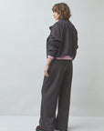SUNCOO coffee brown pants and oversized jacket styled with pink top in a minimalist studio, model turned away.