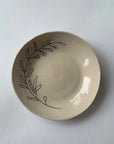The Faire Ring Bowl is a cream-colored ceramic catch-all featuring a simple black line drawing of leafy branches, showcasing botanical symbolism in its design.