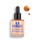 A bottle of Faire Natural Bronzing Serum Sun Radiance, featuring a black dropper cap and orange-tinted serum inside, with two drops displayed next to it on a white background.