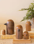 Kalalou teak birds displayed on books next to a green fern in a woven basket, styled for Bungalow Furniture.