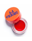 An open container of Faire 03 Tinted Lip Balm & Blush with a bright red tint and an orange lid is viewed from above on a white background.