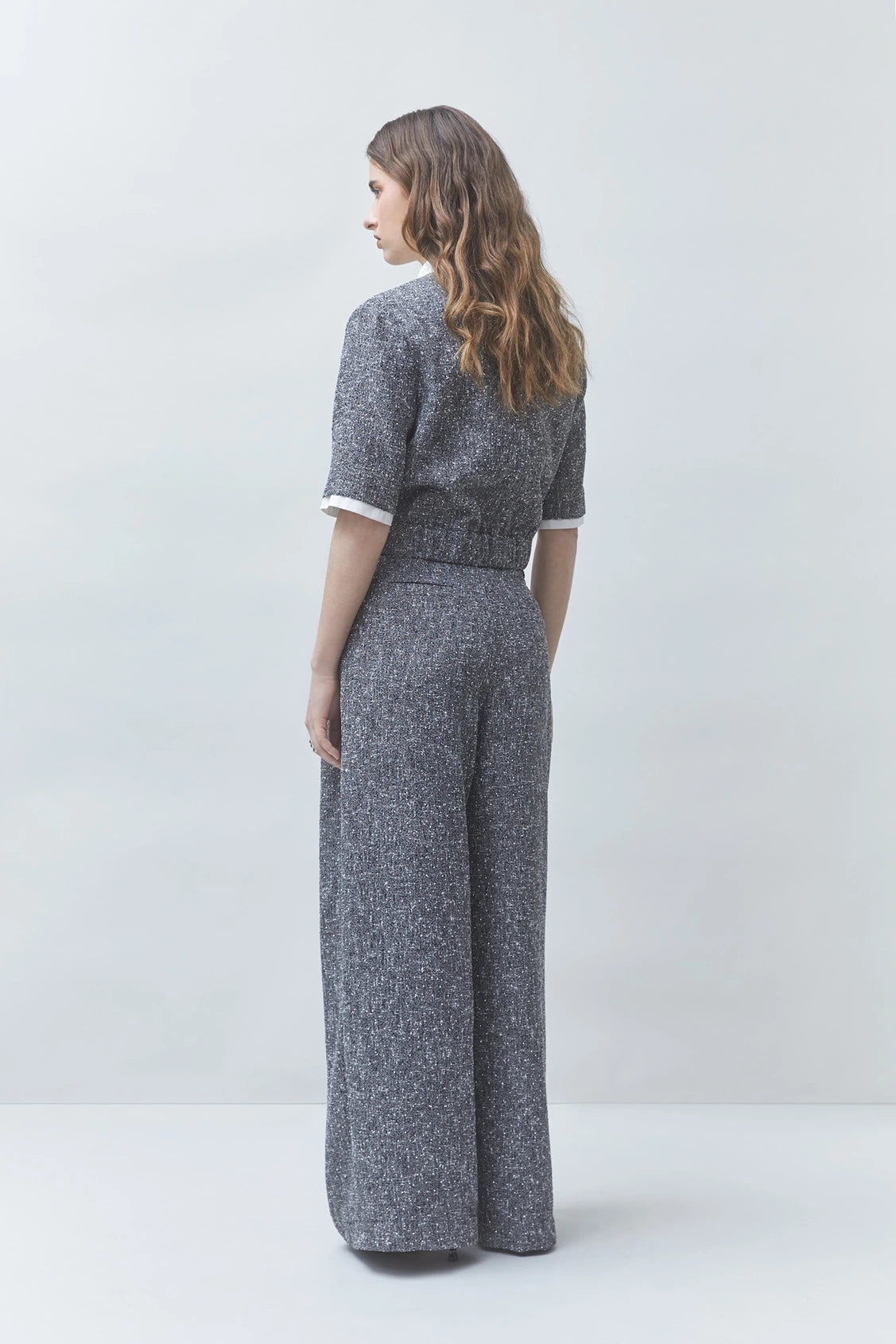 SUNCOO Jerk textured grey jumpsuit and recycled polyester pants modeled from behind, wavy hair adds casual style.