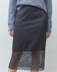 SUNCOO black satin and lace midi Face Skirt with sheer hem, styled with a grey sweater, plain backdrop.