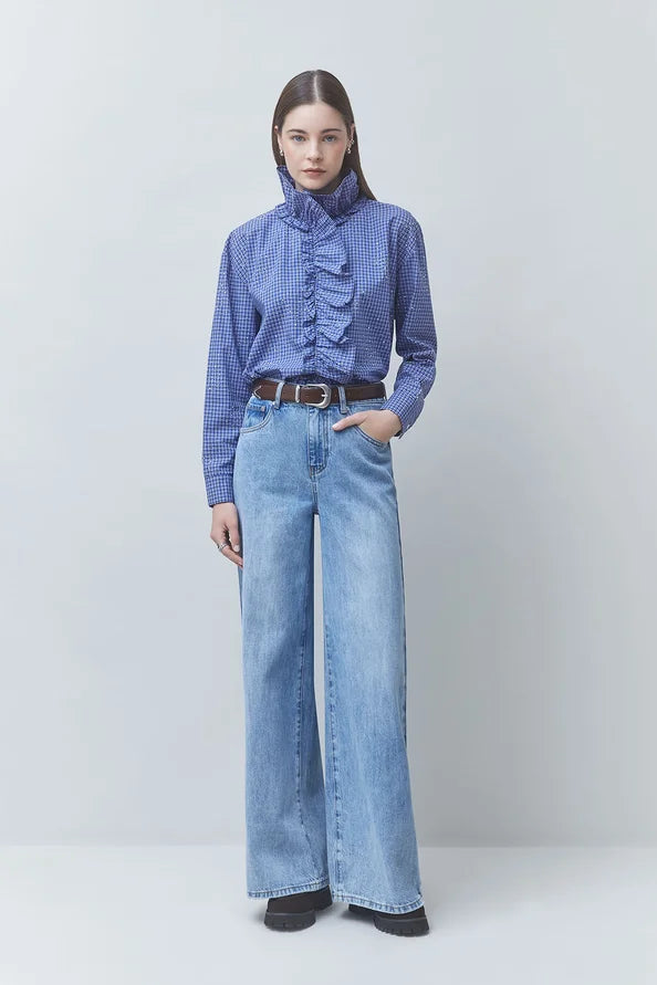 SUNCOO Lyes blue ruffle shirt styled with wide-leg jeans and brown belt, light neutral background.