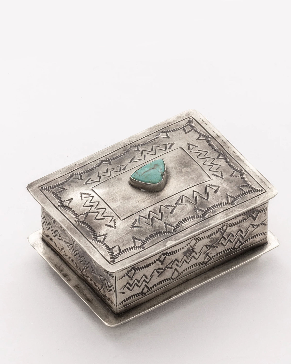 The J Alexander Rustic Silver 15-1-T Small Stamped Box with Turquoise features engraved geometric designs and a central turquoise stone, adding Southwestern elegance. Shown on a plain white background.