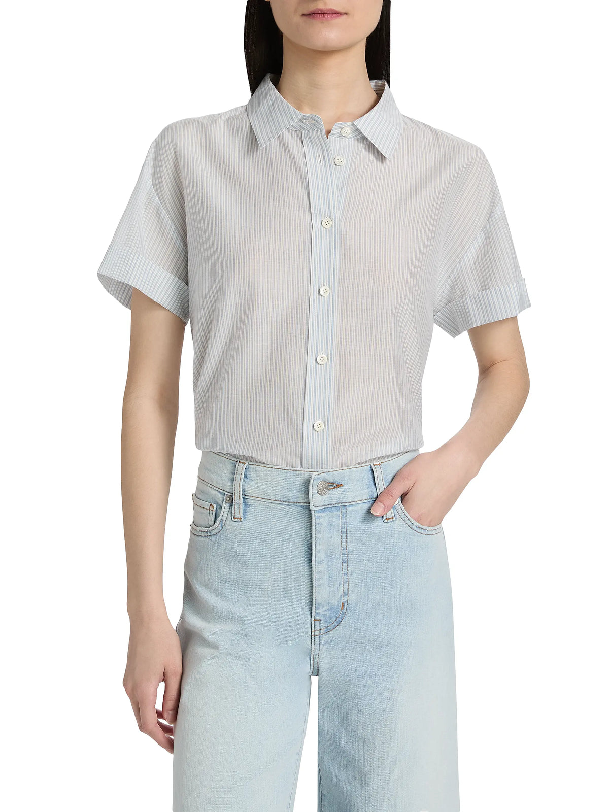 A woman wears the FRAME Boardwalk Shirt in light blue and white stripes, crafted from cotton-silk, tucked into high-waisted, light-wash jeans with one hand in her pocket.